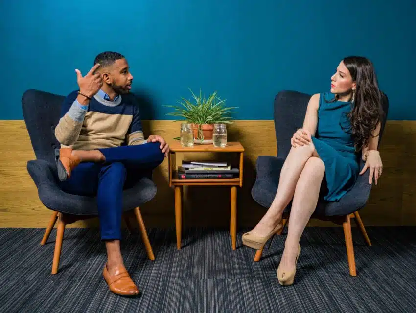 “Two people sit in chairs debating”