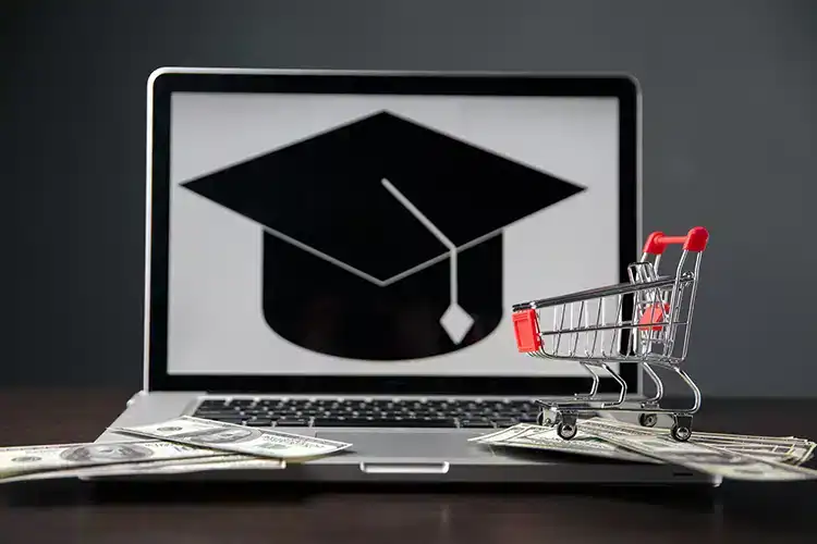 a miniature shooping cart placed next to a laptop screen showcasing a graduation cap
